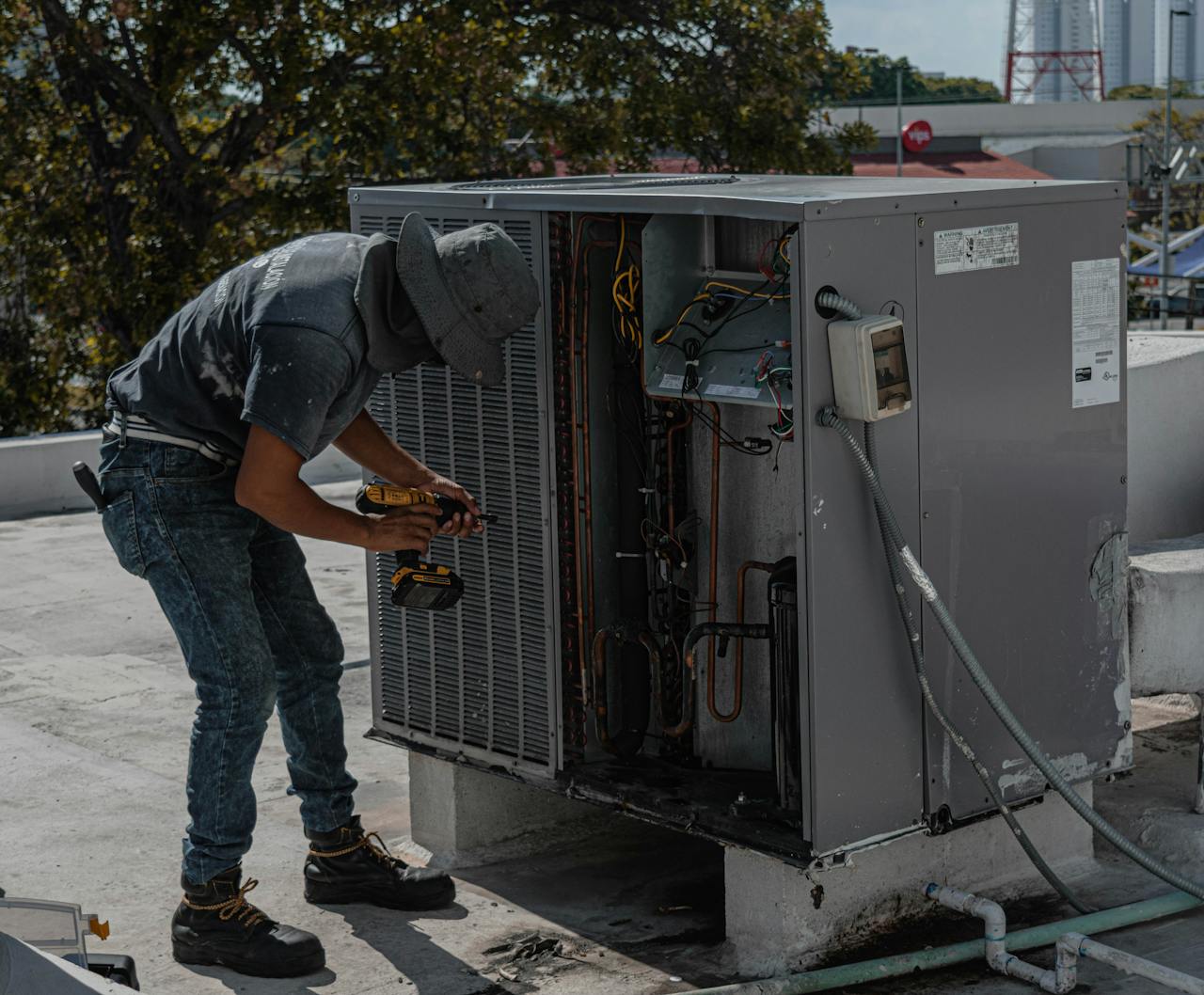 contact-img A worker in a bucket hat repairs an outdoor air conditioning unit on a rooftop.